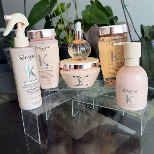 Foto real del kit Kérastase Gloss Absolu con dos shampoos, mascarilla, spray, crema Frizz-Glaze y aceite sobre bases transparentes.