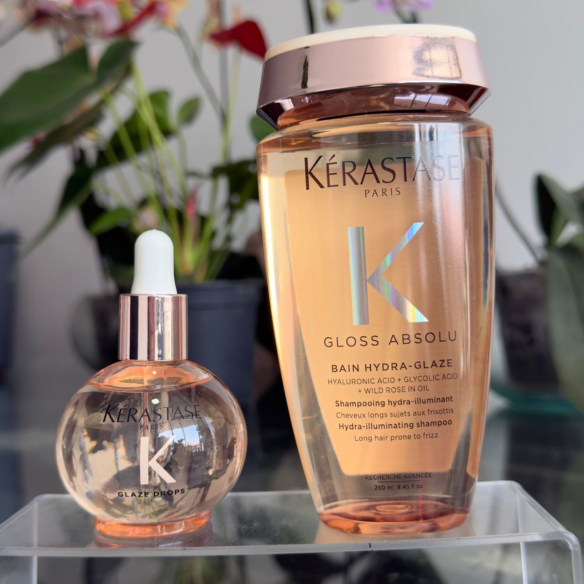 Foto real del dúo Kérastase Gloss Absolu: aceite Glaze Drops junto al shampoo Bain Hydra-Glaze sobre una base transparente.